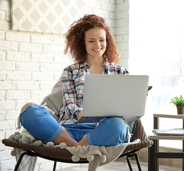 Jeune femme souriante, assise en tailleur avec un ordinateur portable sur les genoux.