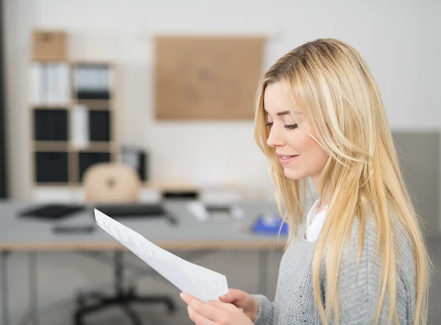 Jeune femme blonde lisant un document dans un bureau moderne.